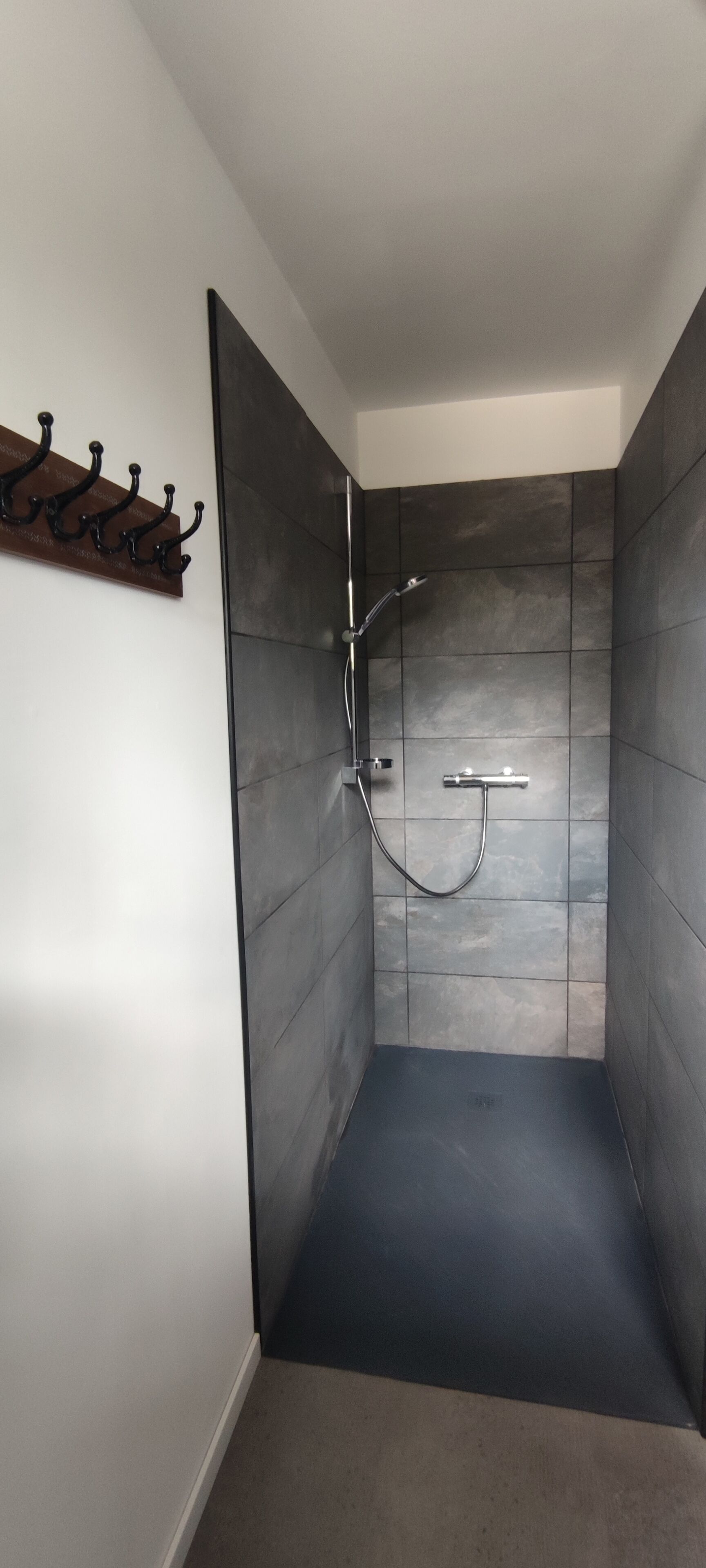 A modern shower with dark tiles and a metal showerhead.