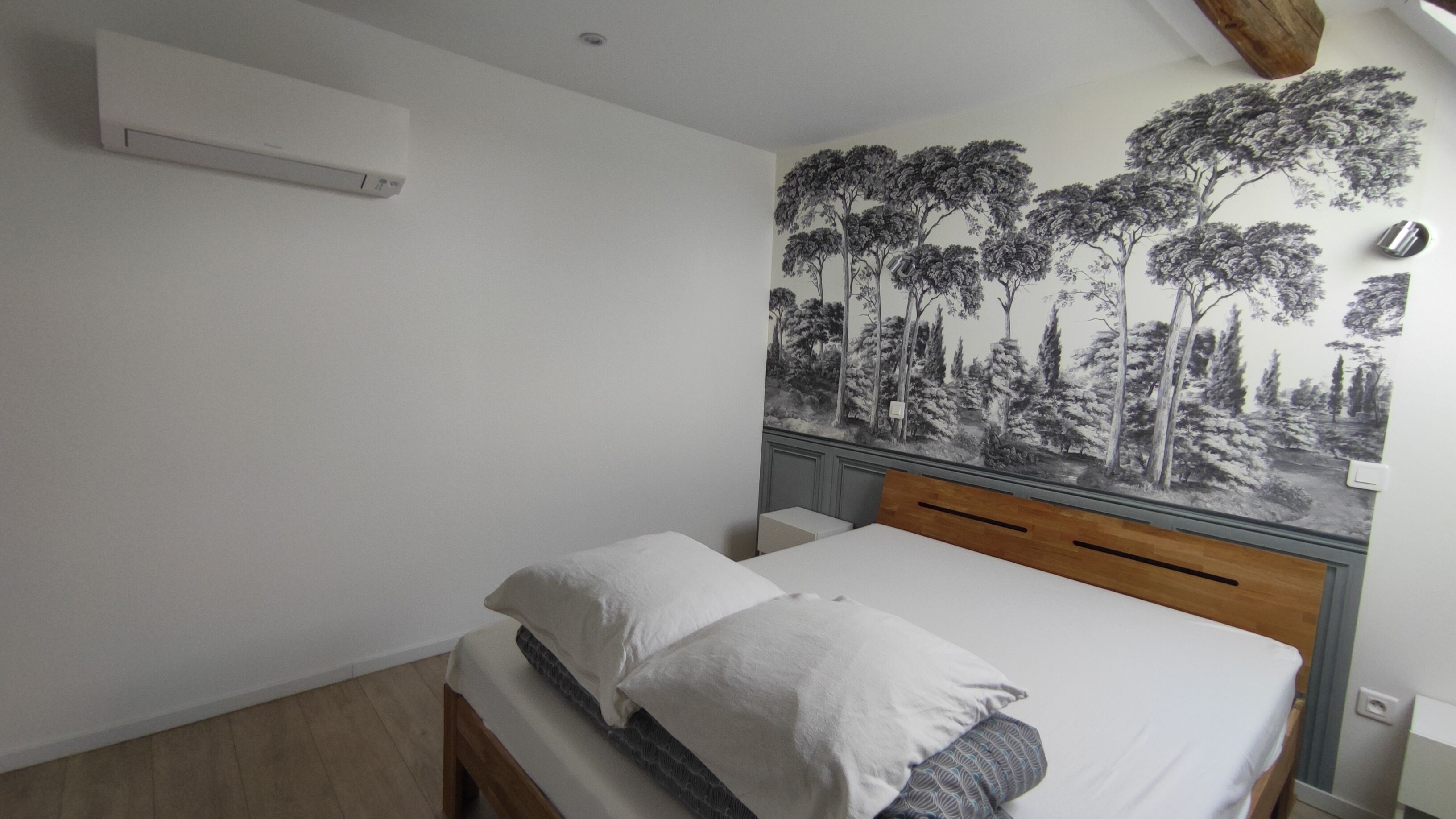 A bedroom with a bed, a wall-mounted air conditioner, and a forest mural.