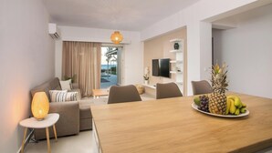 A modern living room with a sofa, a dining table with fruit, and a TV.