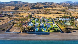 An aerial view of a coastal resort with multiple buildings, a beach, and mountains in the background.