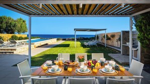 An outdoor dining area with a view of the sea, a pool, and a well-maintained lawn.