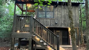 Une cabane rustique dotée d’une terrasse en bois, d’un escalier et d’un petit espace porche.