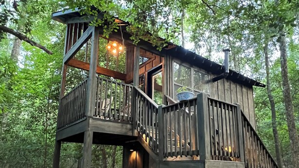 Une cabane en bois dotée d’un balcon, d’une cheminée et d’un coin repas.