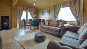A cozy cabin interior with a fireplace, wooden walls, a sofa, a dining table, and a rug. - Stag Lodge - UK46921 (Falkirk)