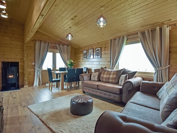 A cozy cabin interior with a fireplace, wooden walls, a sofa, a dining table, and a rug.