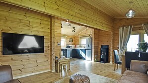 A wooden cabin interior with a TV, sofa, ottoman, kitchen, and dining area. - Stag Lodge - UK46921 (Falkirk)