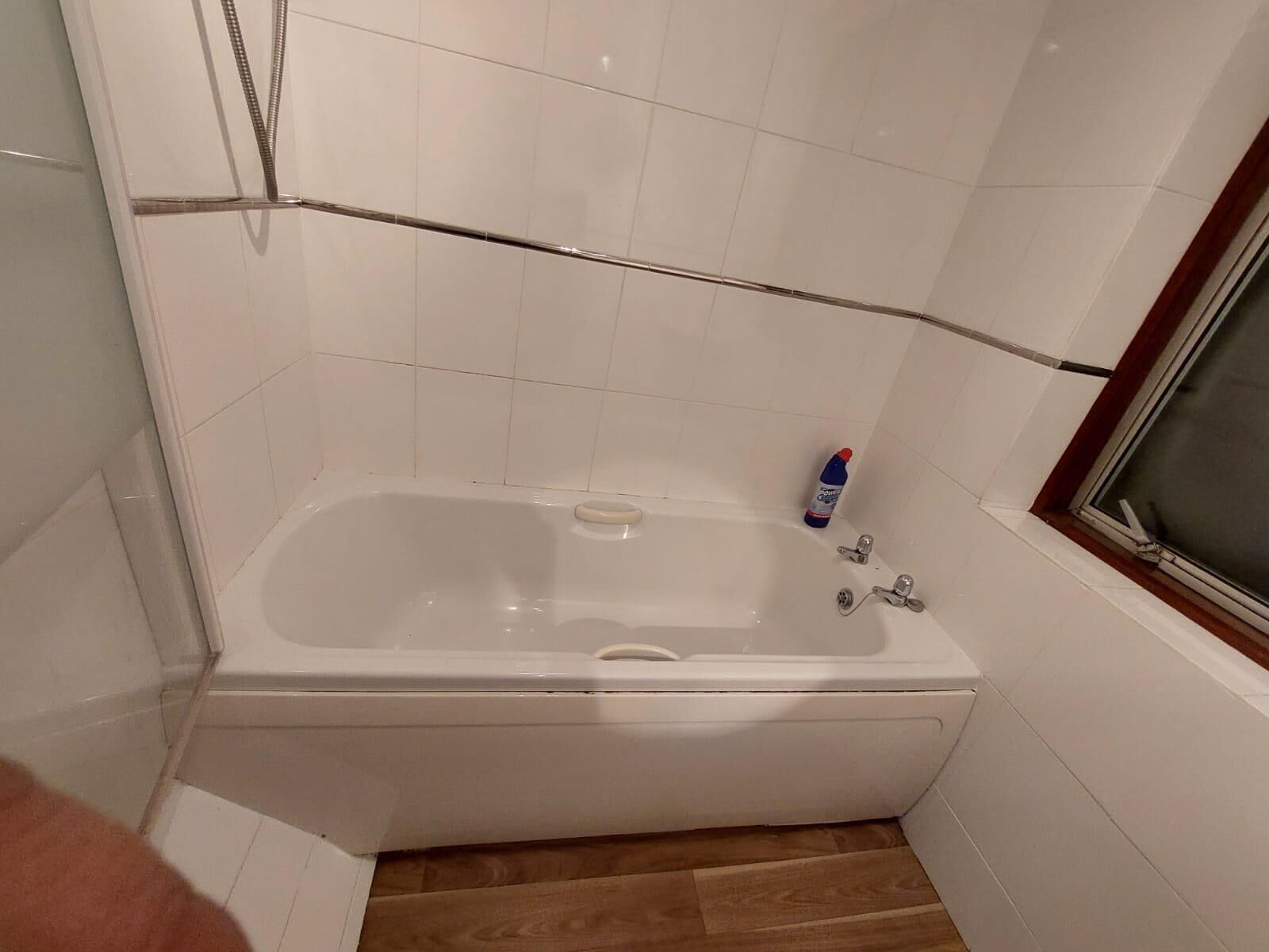 Une salle de bain avec une baignoire blanche, un plancher en bois et une fenêtre avec un cadre en bois.