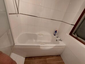 A bathroom with a white bathtub, a wooden floor, and a window with a wooden frame. - Birmingham Blissful Retreat With 3 Bedrooms (Birmingham)