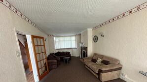 A living room with a brown carpet, two sofas, a fireplace, and a clock on the wall. - Birmingham Blissful Retreat With 3 Bedrooms (Birmingham)