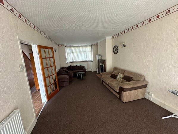 A living room with a brown carpet, two sofas, a fireplace, and a clock on the wall. - Birmingham Blissful Retreat With 3 Bedrooms (Birmingham)