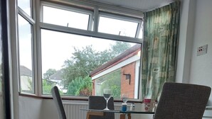 A dining area with a table and four chairs, a window with a view of a house, and a power outlet on the floor. - Birmingham Blissful Retreat With 3 Bedrooms (Birmingham)