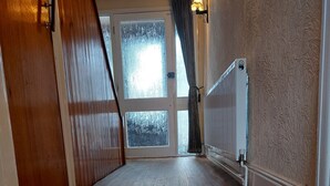 A hallway with wooden flooring, a door on the left, a radiator on the right, and a window at the end. - Birmingham Blissful Retreat With 3 Bedrooms (Birmingham)
