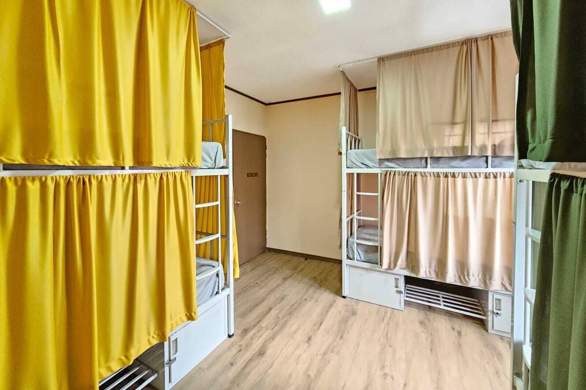 A dormitory room with bunk beds, wooden flooring, and curtains.