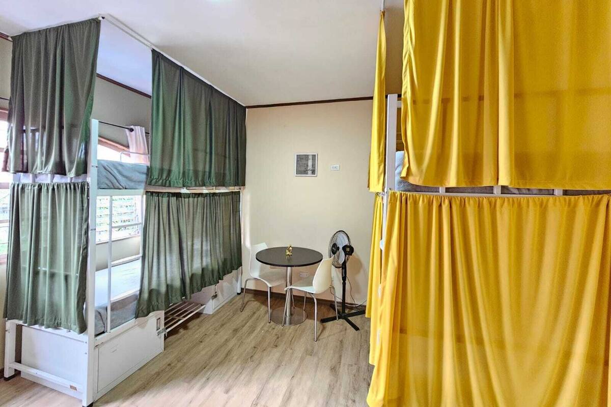 A room with bunk beds, a small table, a fan, and a window with curtains.