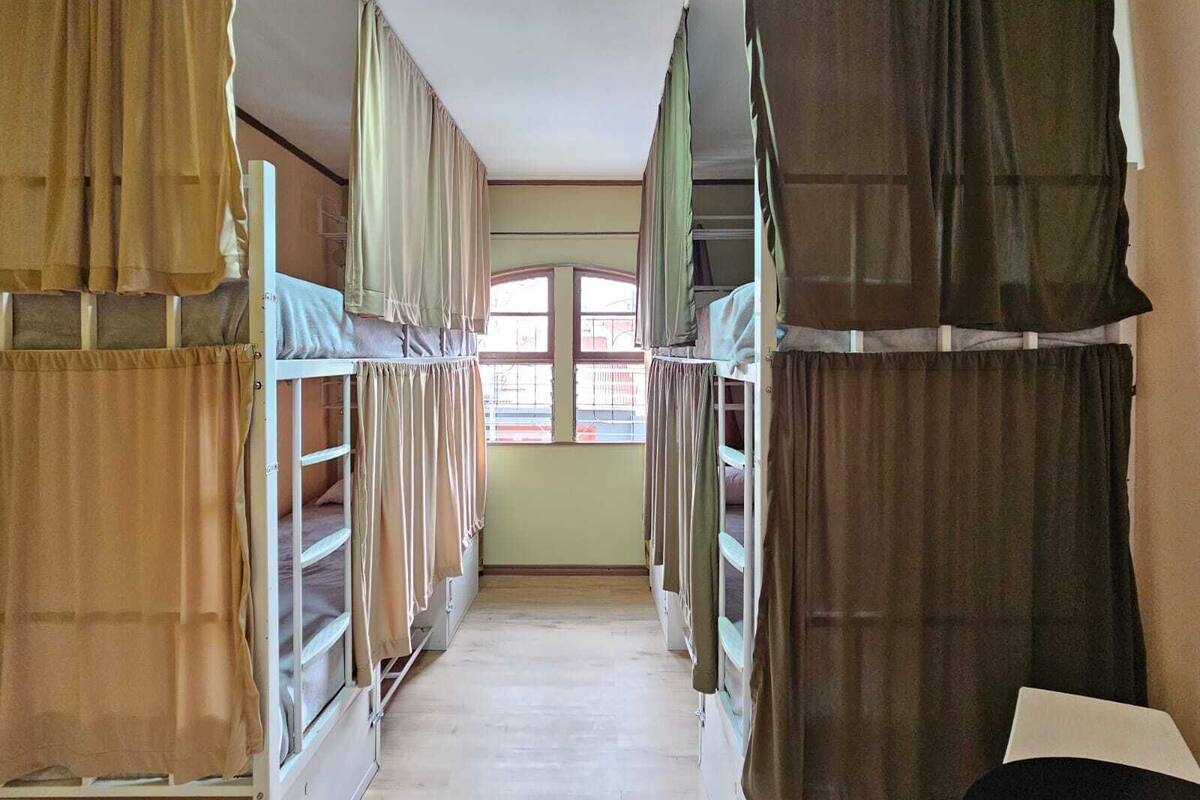 A narrow corridor with bunk beds on either side, a window at the end, and a ceiling light.