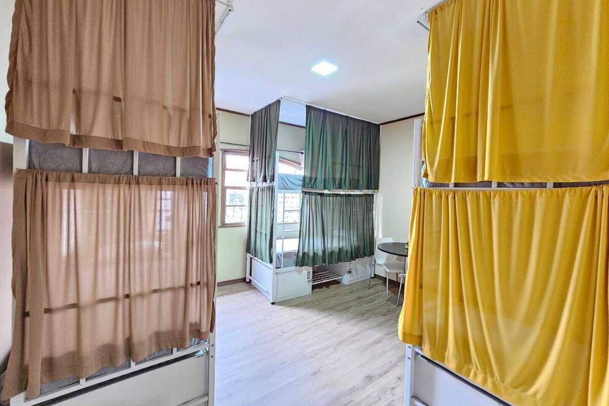 A room with a bed, a desk, and a chair. There are curtains on the windows.