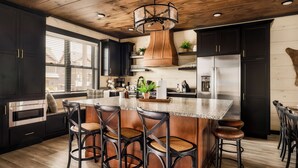 A modern kitchen with dark cabinetry, a central island with stools, stainless steel appliances, and a wooden ceiling.