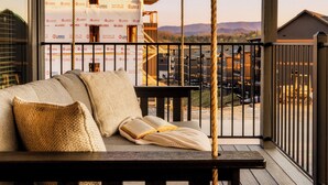 A wooden deck with a swing seat and rope, overlooking a building under construction.