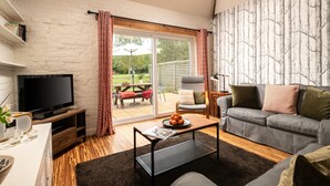 Ein Wohnzimmer mit Fernseher, Sofa, Couchtisch und einer Schiebetür zu einem Außenbereich.