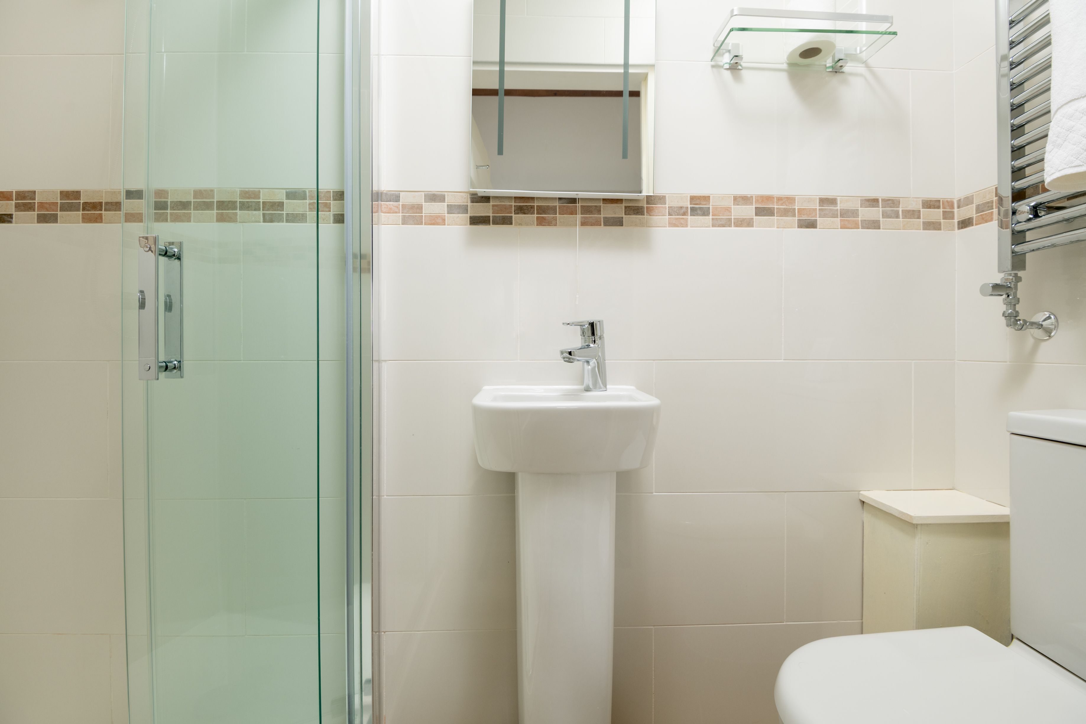 A bathroom with a glass shower enclosure, a pedestal sink, a toilet, and a mirror above the sink.