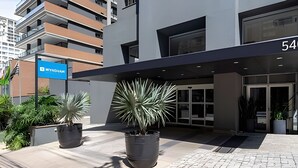 A modern building with a large entrance, potted plants, and a sign indicating a hotel. - Get a Flat 805 Região Jardins SP (São Paulo)