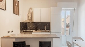 Cocina moderna con salpicadero de mármol, armarios blancos y una isla central con dos sillas negras.
