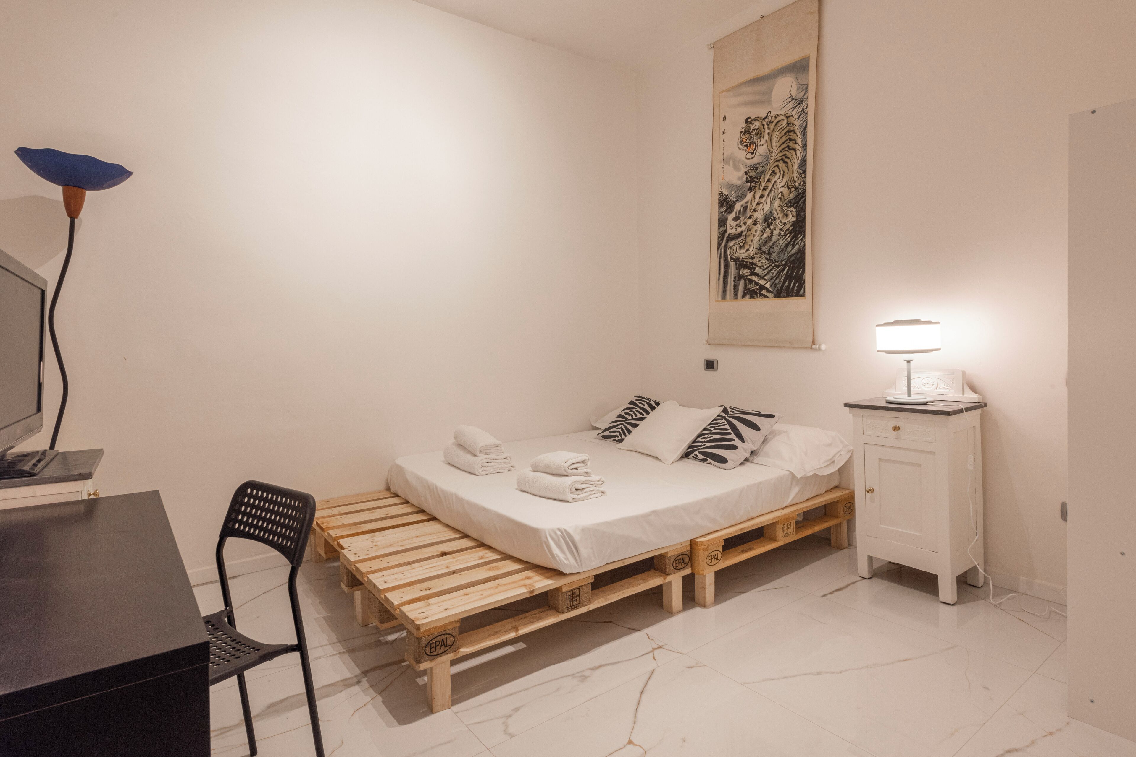 A minimalist bedroom with a wooden bed, a desk, a chair, and a small cabinet.