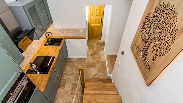 A modern kitchen with green cabinets, a wooden countertop, and a built-in stove. A wooden staircase leads to a door with a tree design. - Vysoke nad Jizerou Kds007 (Vysoké nad Jizerou)