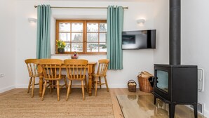 A cozy room with a wooden dining table and chairs, a large window with curtains, a black wood-burning stove, and a mounted TV. - Vysoke nad Jizerou Kds007 (Vysoké nad Jizerou)