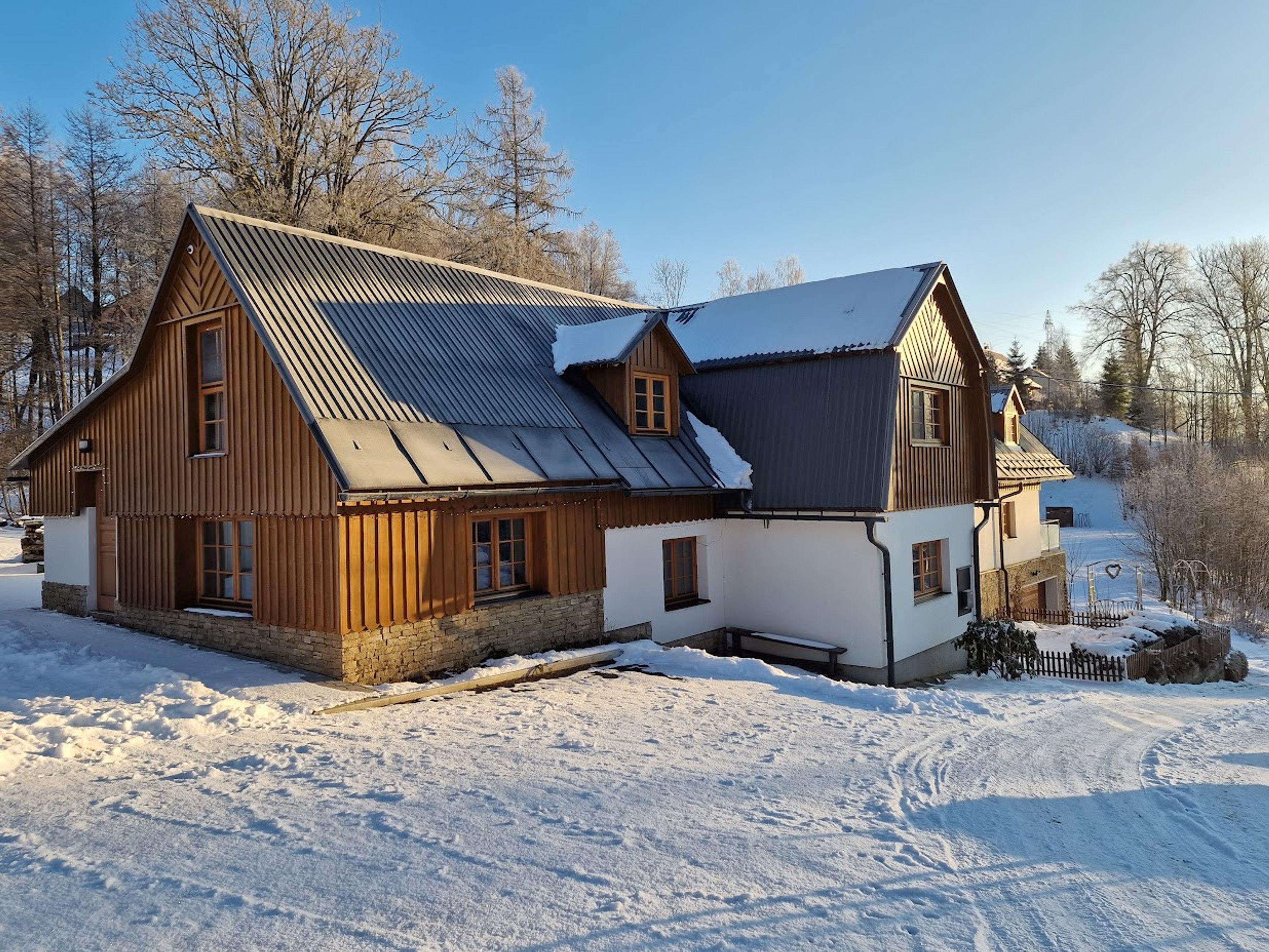 A large wooden house with a metal roof, surrounded by snow-covered ground and trees.