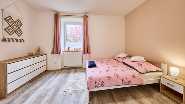 Un dormitorio con cama, mesita de noche y ventana con cortinas.