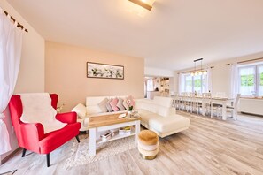 Una sala de estar moderna con un sillón rojo, un sof á blanco y una mesa de centro de madera. En el fondo, se ve un área de comedor con una mesa y sillas blancas.