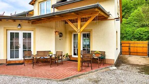 Ein Haus mit einer überdachten Terrasse, Holzmöbeln und einem Ziegelfußboden.