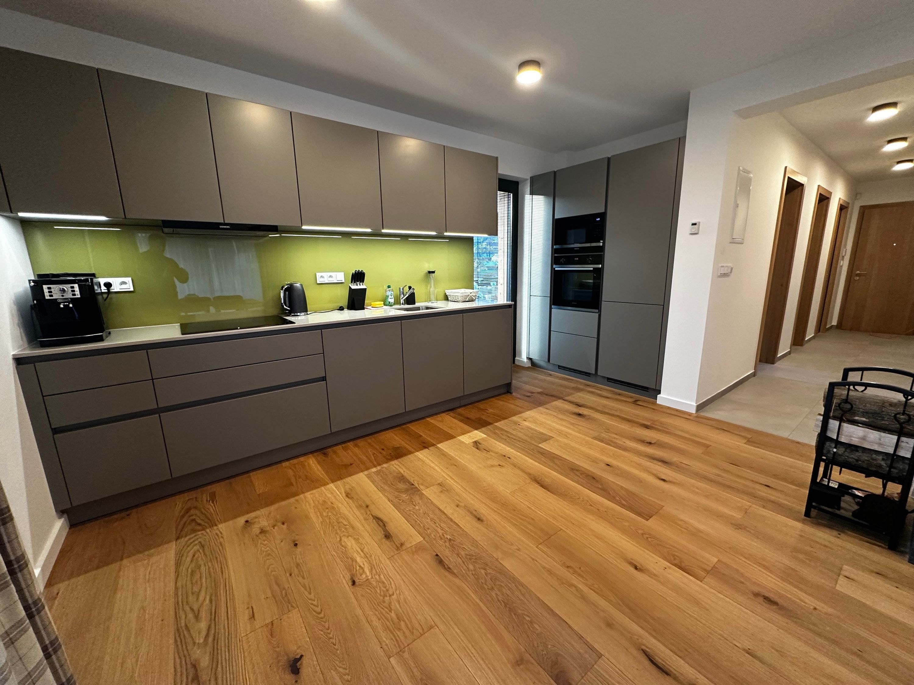 A modern kitchen with grey cabinets, a wooden floor, and a built-in oven.