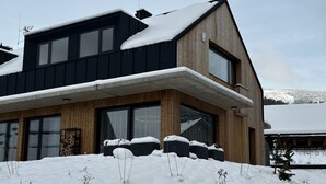 A modern two-story house with a sloped roof covered in snow, large windows, and a stone foundation. - Cerny Dul Kcb045 Villa (Cerny Dul)