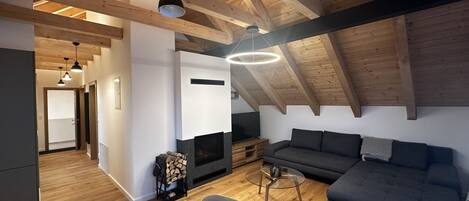 A modern loft with exposed wooden beams, a fireplace, a sofa, and a dining area with chairs.