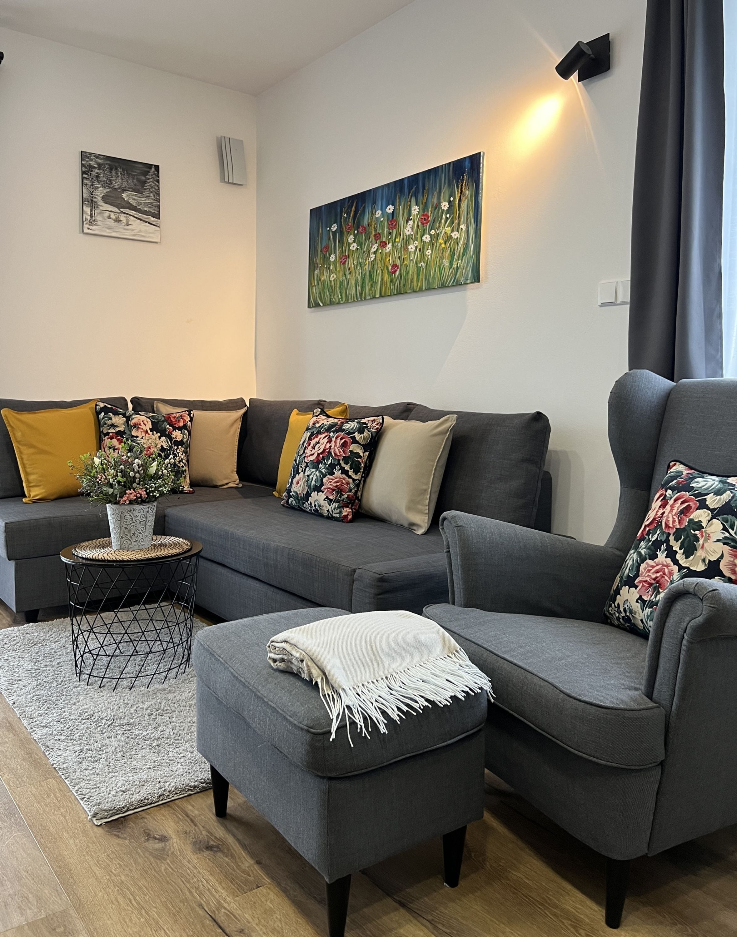 A modern living room with a sectional sofa, a small round table with a vase, a decorative rug, and two wall-mounted paintings.