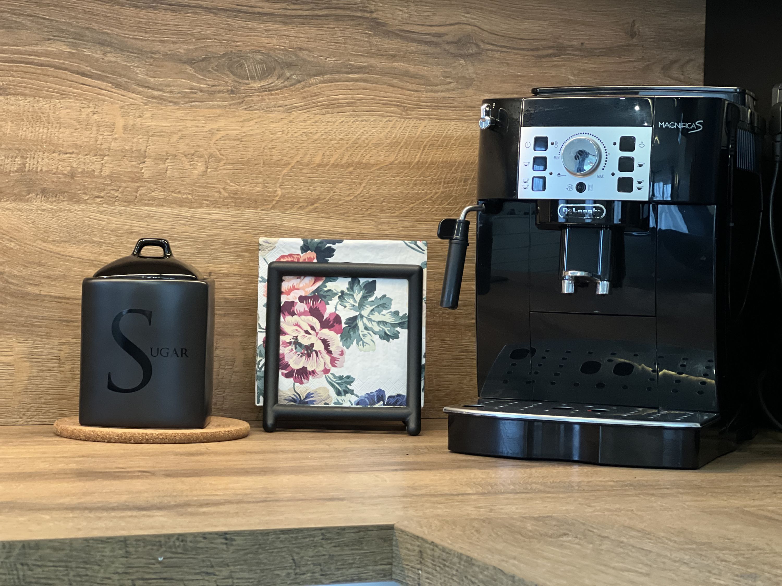 Une machine à café, un récipient à sucre et un tableau encadré, le tout posé sur une surface en bois.