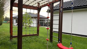 A wooden swing set with a netted overhead structure.