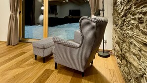 Ein gemütliches Zimmer mit einem hundszahn-Muster Sofa, Holzboden, einer Steinwand und einer großen Glasschiebetür, die zu einem verschneiten Außenbereich führt.