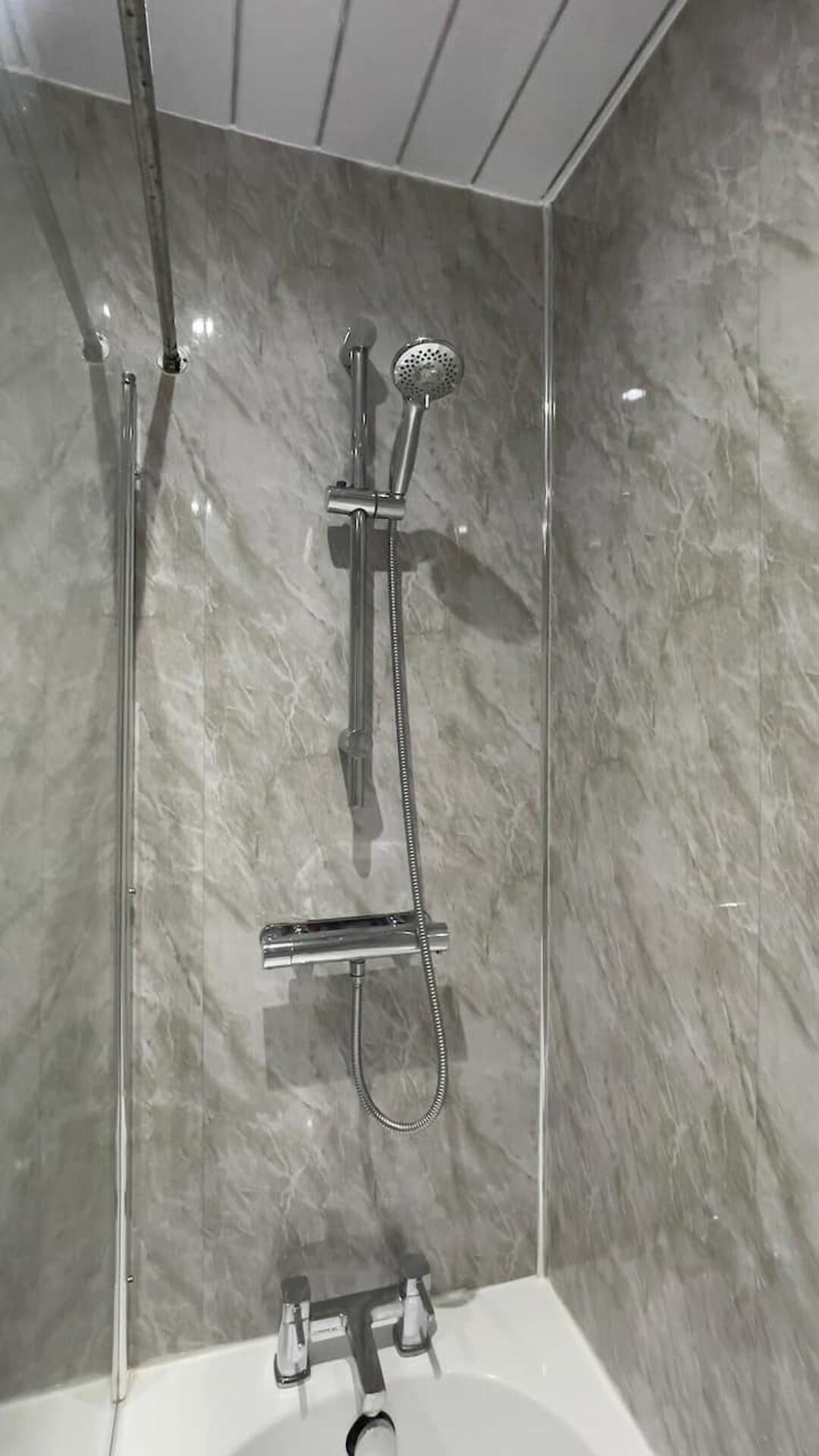 A modern bathroom with a glass-enclosed shower, a standalone bathtub, and a marble wall.