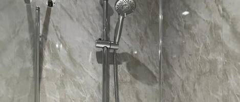 A modern bathroom with a glass-enclosed shower, a standalone bathtub, and a marble wall.