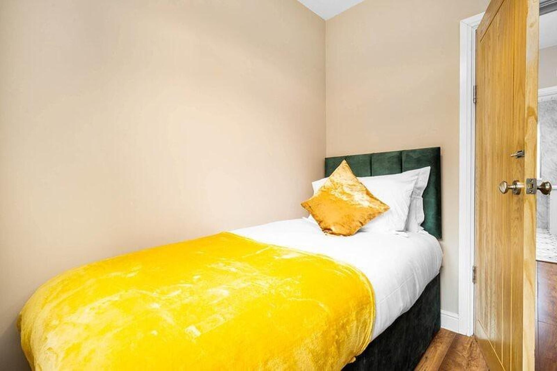 A single bed with a yellow bedspread and a green headboard in a room with beige walls.