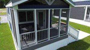 A covered patio area with a table and chairs, a small staircase leading up to the entrance, and a view of the surrounding lawn and buildings. - Lake View Cabin, 2 Bedrooms, 13 miles from Jacksonville! (Maysville)