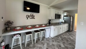 A modern kitchen with a granite countertop, white cabinets, a stainless steel refrigerator, a microwave, and a flat-screen TV mounted on the wall. - Lake View Cabin, 2 Bedrooms, 13 miles from Jacksonville! (Maysville)