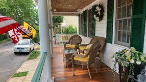 A porch with wicker chairs and a table, a flag, and a statue of a girl holding a tray. - Spend Commissioning Week Here:  Walk to Yard, Pool, Hot Tub, Kayaks, and more... (Annapolis)