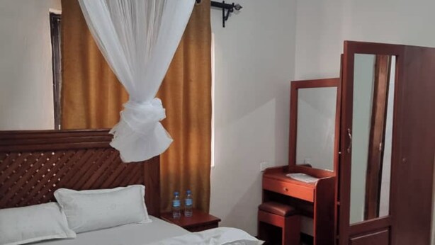 A hotel room with a bed, a nightstand, a wooden dresser, a mirror, and a canopy over the bed. - Voyage Camp Safari Lodge (Arusha)