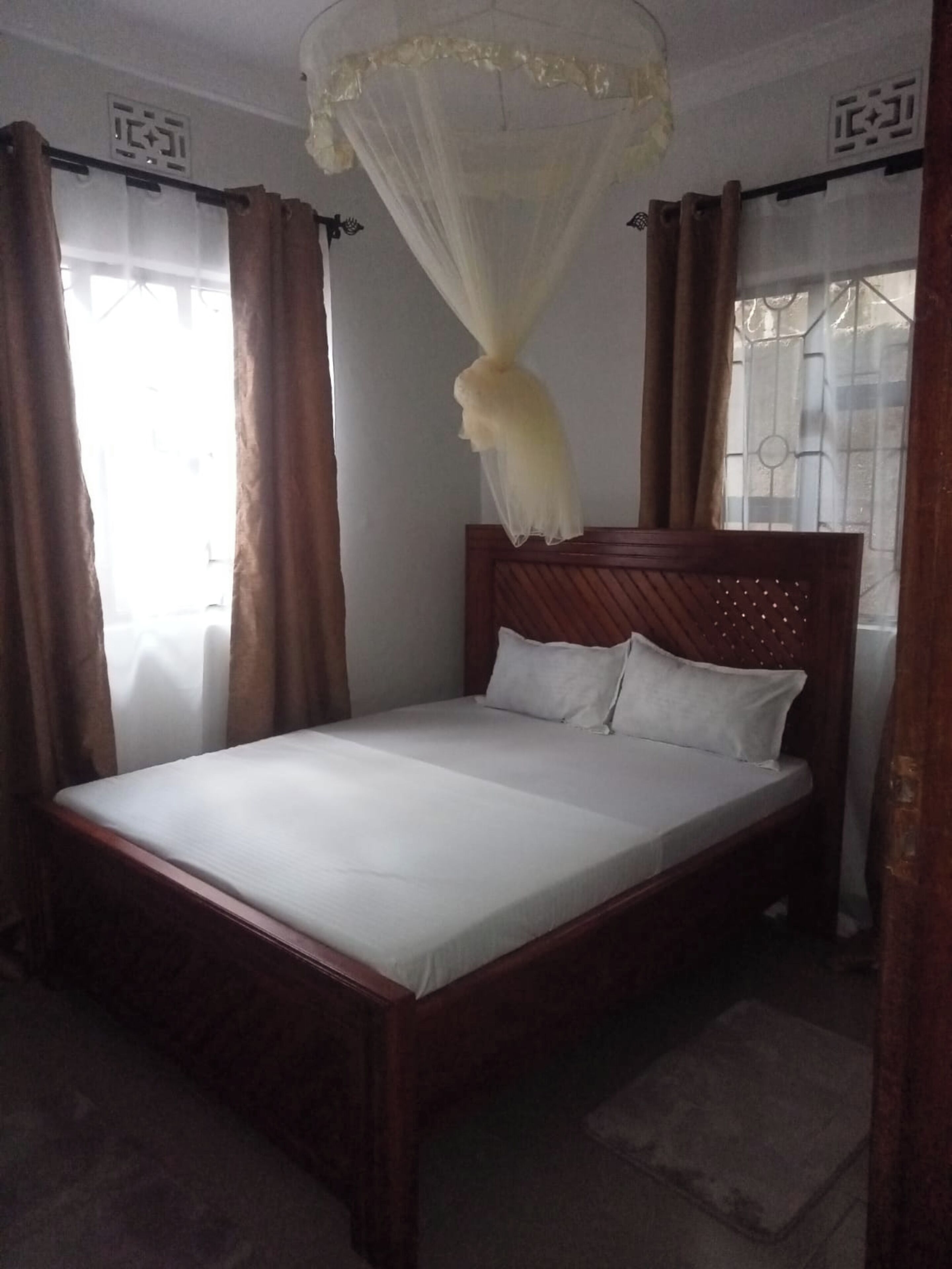 A single bed with a wooden frame and white bedding, a canopy with a white net, and brown curtains.