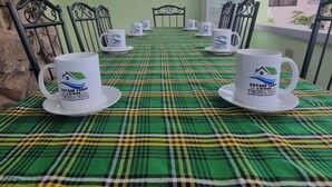 A conference room with a green plaid tablecloth, six white coffee cups with logos, and black metal chairs. - Voyage Camp Safari Lodge (Arusha)