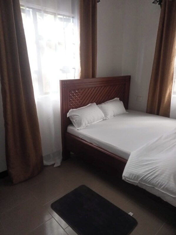 Una cama individual con cabecera de madera, ropa de cama blanca y un tapete negro en el suelo.